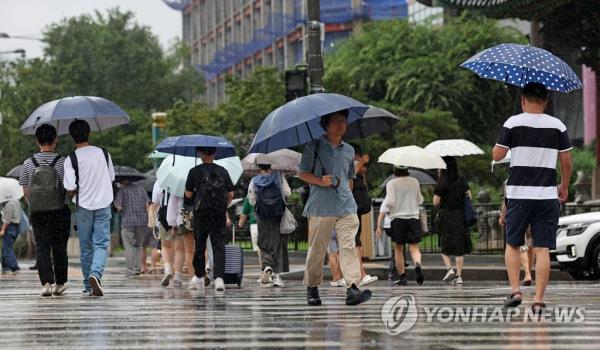 People holding umbrellas walk across a crosswalk in central Seoul on July 23, 2023, as a heavy rain watch has been issued for the capital city. (Yonhap)